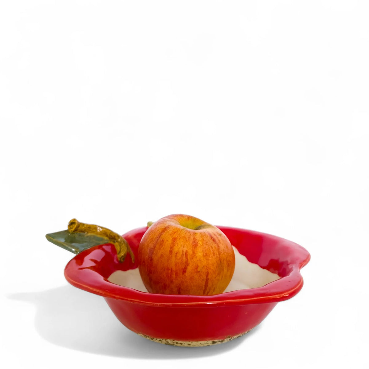 Red apple-shaped baker bowl holding an apple, with a cream interior and green leaf accent, viewed from the side