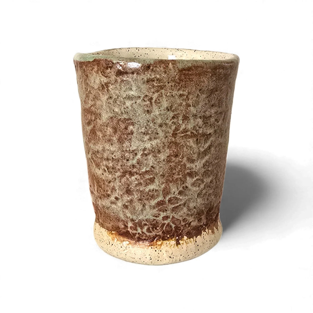 Handcrafted stoneware tumbler with mottled brown and cream glaze, a speckled cream interior, and an unglazed base.
