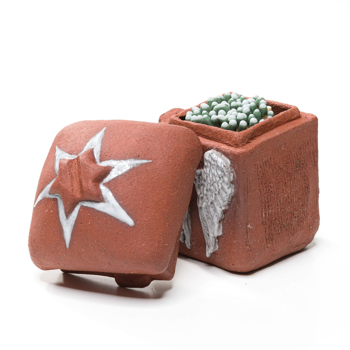 Open stoneware angel-wing matchbox filled with green-tipped matches, with its star-decorated lid leaning beside it