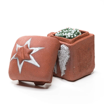 Open stoneware angel-wing matchbox filled with green-tipped matches, with its star-decorated lid leaning beside it
