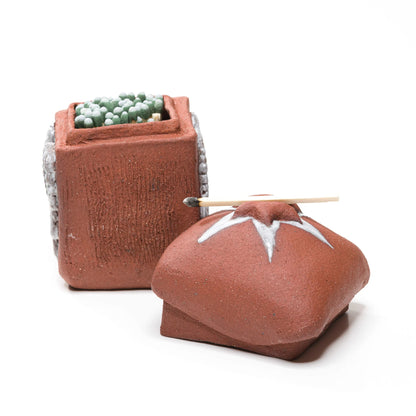 Open reddish-brown stoneware matchbox filled with matches, with a single match resting across the detached star-topped lid