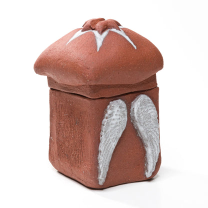 Closed stoneware matchbox viewed at an angle, showing raised white angel wings, a textured side and a star-topped lid