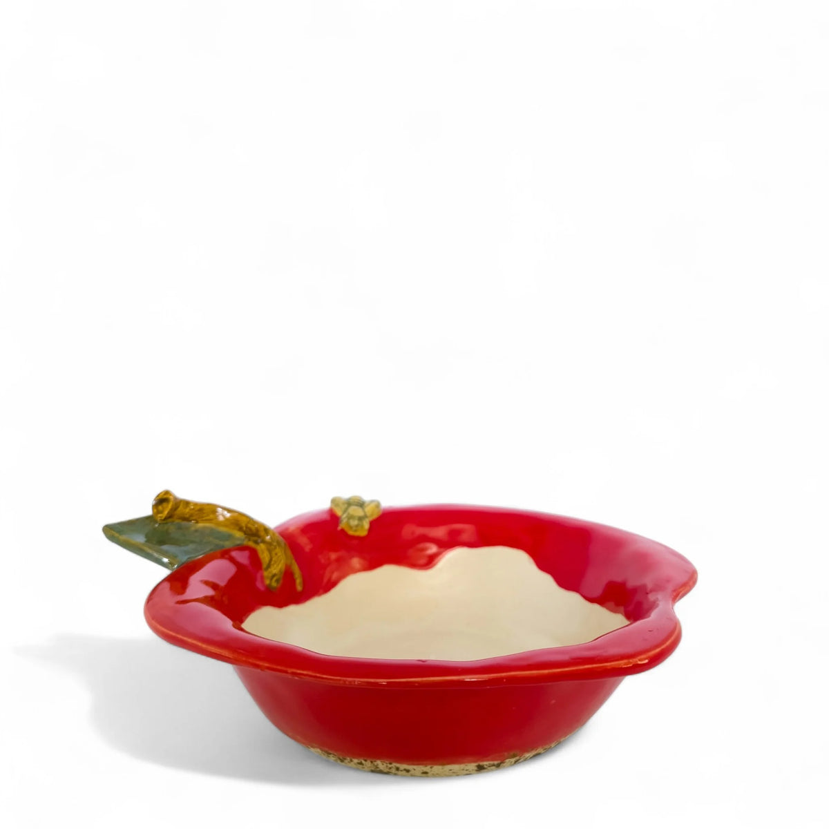 Empty red apple-shaped baker bowl with cream interior, green leaf, and small bee detail, viewed from the side