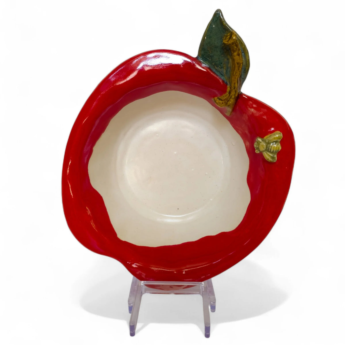 Red apple-shaped baker bowl with cream interior, green leaf, and small bee detail, displayed upright on a stand