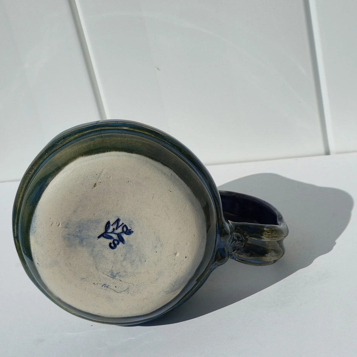 Underside of the stoneware mug showing its unglazed base and blue maker’s mark