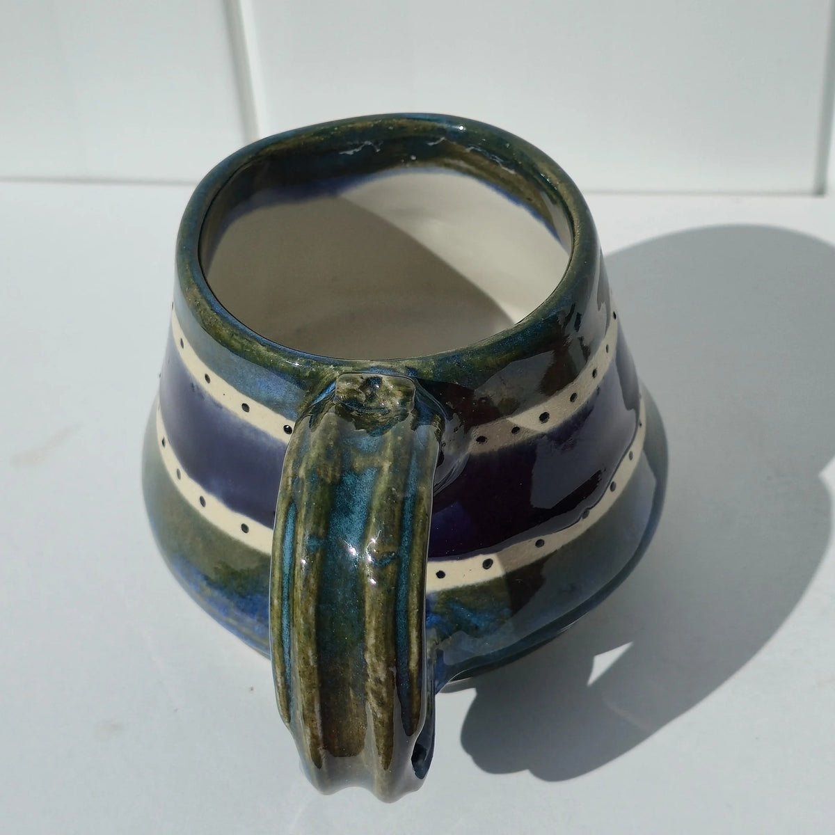 Close-up of the green glazed handle on a green and indigo striped stoneware mug