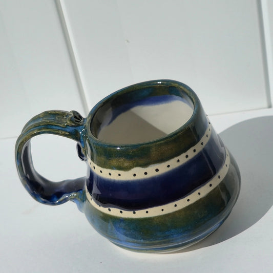 Green and indigo striped stoneware mug with cream dotted bands and the handle on the left
